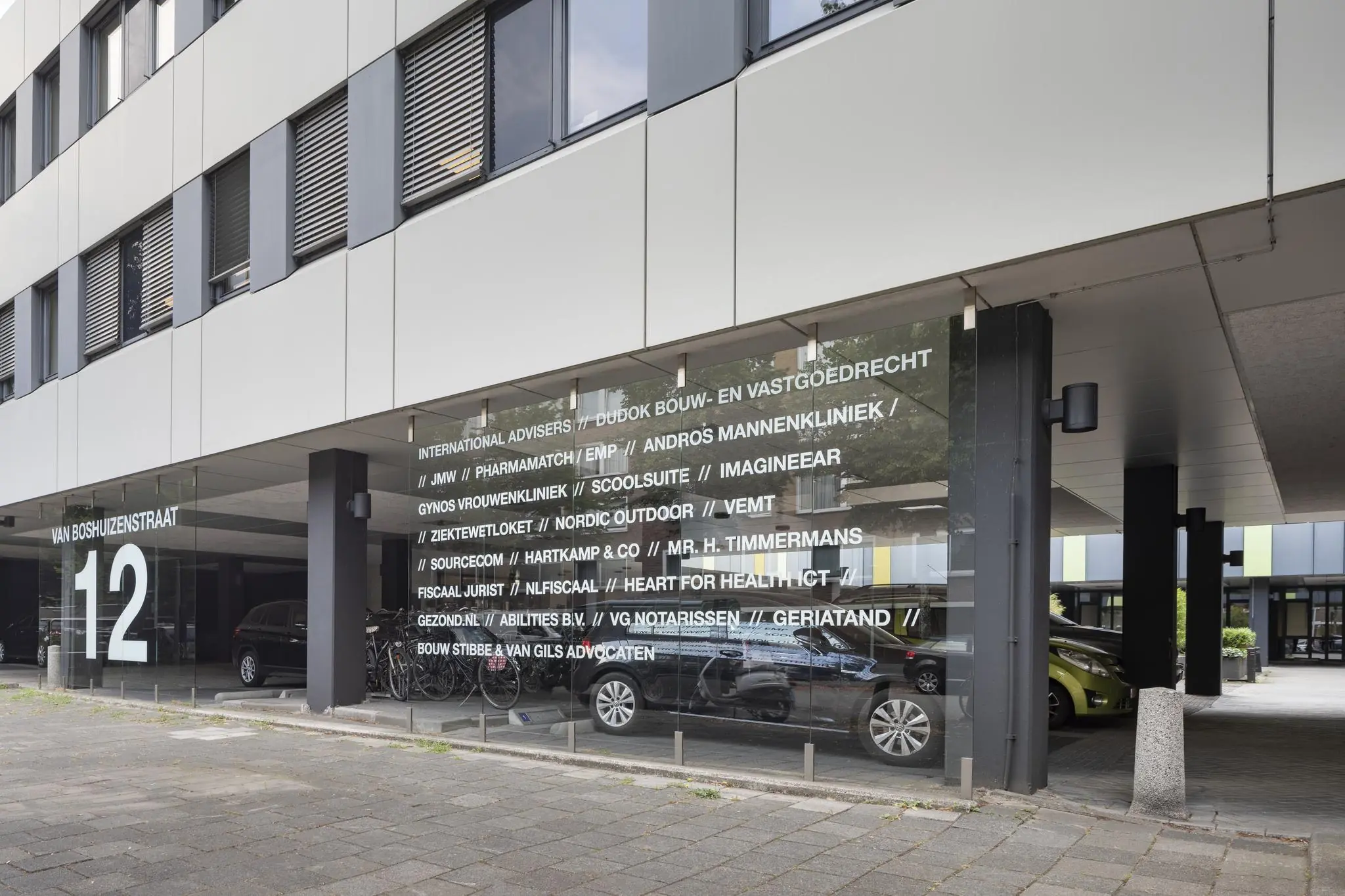 Ingang van een kantoorgebouw aan de Van Boshuizenstraat 12 met bedrijfsnamen op glazen gevel.